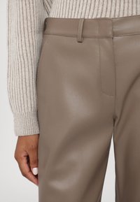 Brune faux skinnbukser med en glatt tekstur, med standard midjebånd, frontlomme og slim fit, kombinert med en ribbet gensererm.