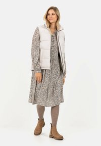 Polstret letvægtsvest i lys grå, båret over en blomsterkjole. Brune ankelstøvler fuldender outfittet, som har en tætsiddende talje og en svajet nederdel.