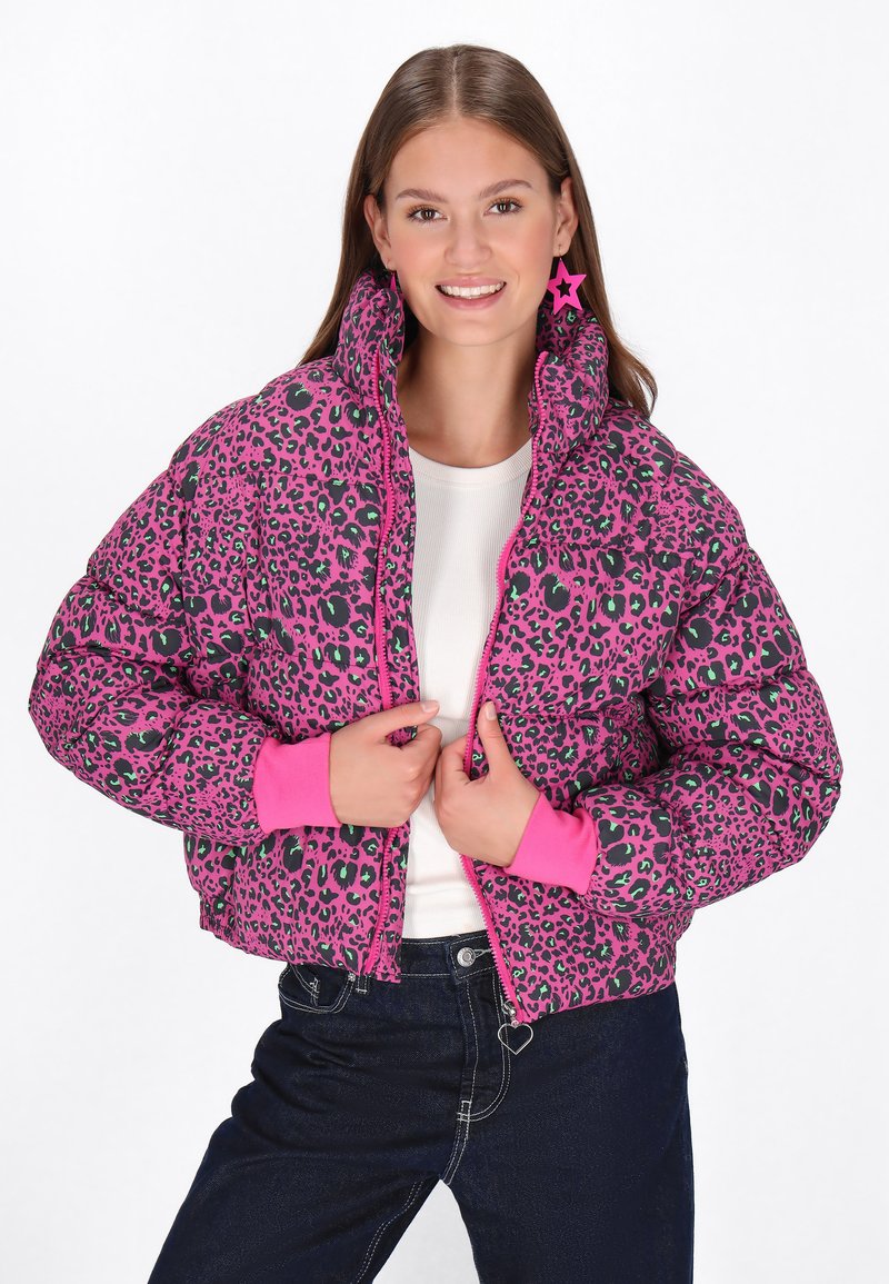 Jachetă pufă cu imprimeu leopard roz, cu accente negre, manșete striate și guler înalt; asortată cu un top alb și blugi închisi la culoare.