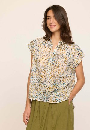 Blouse à manches courtes, boutonnée, en tissu léger et transparent avec un motif floral jaune et bleu sur fond blanc.