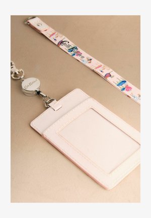 Jasnoróżowy etui na karty z przezroczystym okienkiem na identyfikator, przymocowany do zwijanego smycza Cath Kidston z wzorami kwiatów i sukienek.