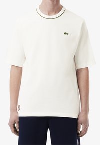 T-shirt bianco a maniche corte con colletto a contrasto, logo ricamato verde sul lato sinistro del petto e etichetta sul lato inferiore. Tessuto di cotone morbido.