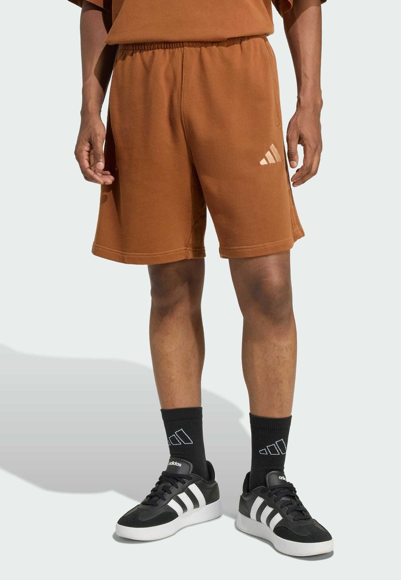 Hnedé bavlnené šortky s elastickým pásom, s malým bielym logom Adidas. Doplnenej čiernymi ponožkami a teniskami.