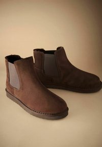 Bruna mocka ankelskor med elastiska sidopaneler och texturerade gummisulor, med en slät yta och rundad tådesign.