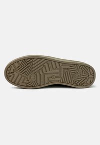 Suela de un zapato en marrón claro con un patrón texturizado, que presenta surcos y formas para mejorar la tracción. Incluye marcaciones para la sostenibilidad y el tamaño.