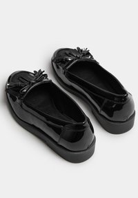 Svarta lackskor med rund tå, en texturerad gummisula och en dekorativ rosett av satinband framtill.