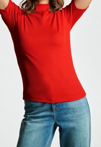 Rød ribbet kortærmet top med en mock neckline, tætsiddende design og glat tekstur, parret med lyseblå denimjeans.