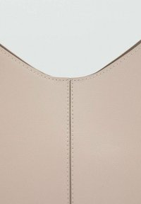 Finta pelle beige con una texture liscia, presenta un collo a V e una cucitura centrale, messa in risalto da cuciture a contrasto.