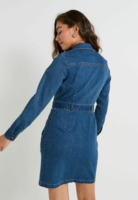 Vestido de denim con cuello estructurado, mangas largas y cintura ajustada. La tela es de un azul oscuro con detalles de costura visibles.