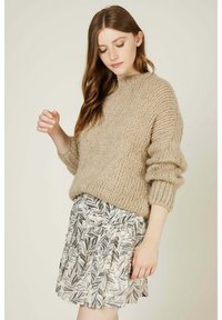 Pull en tricot beige avec un col rond et des manches surdimensionnées, associé à une jupe plissée noir et blanc à motif de feuilles.