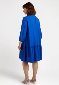 Abito blu a lunghezza ginocchio con fondo a strati, maniche a sbuffo e una vestibilità rilassata. Tessuto morbido e leggero con una texture liscia.