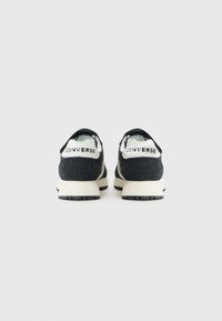 Zwarte suede sneakers met een witte rubberen zool en achtertab. Heeft contrasterende accenten en een logo op de hak. Minimalistisch ontwerp.