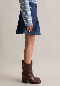 Gonna a trapezio in denim con lavaggio blu scuro, abbinata a stivali ankle in pelle marrone con tacco a blocco e finitura testurizzata.