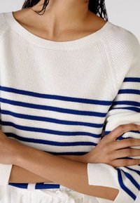 Pull en tricot avec des rayures horizontales bleues et blanches, texture côtelée et col bateau. Les manches ont des détails côtelés aux poignets.