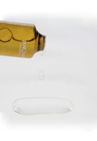 Botella ámbar con cuentagotas inclinada, liberando una gota de líquido claro sobre una mancha de gel translúcido sobre un fondo blanco.