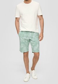 T-shirt beige chiaro abbinato a pantaloni corto verde menta con un motivo foglioso bianco. Modello con scarpe da ginnastica bianche. Outfits estivo casual.