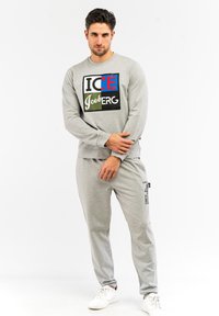Grauer Sweatshirt mit einem mehrfarbigen "ICE IceBERG"-Grafik, kombiniert mit grauen Jogginghosen mit Logoprint, getragen mit weißen Sneakers.