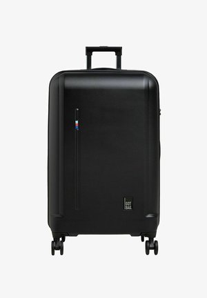 Valigia nera rigida con manico telescopico, quattro ruote, superficie testurizzata, tasca laterale con zip e un piccolo etichetta con logo.