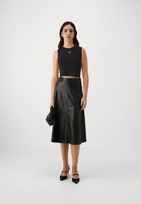 Top negru crop, fustă midi din piele neagră și pantofi negri cu toc înalt. Design simplu, cu texturi netede și detalii subtile ale logo-ului.