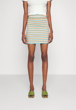 Jupe mini rayée en bleu, orange et blanc en tissu ribbed. Design ajusté, longueur mi-cuisse, assortie à des sandales vertes à enfiler.