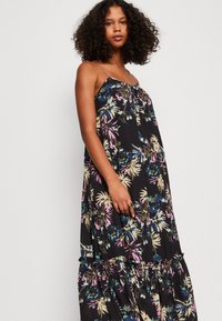 Blumiges Maxikleid mit Spagettiträgern, auf schwarzem Hintergrund mit mehrfarbigen Blümchenmustern und Rüschendetails am Saum.
