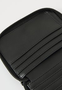 Portefeuille noir à fermeture éclair avec plusieurs emplacements pour cartes, présentant une texture lisse et des accents cousus. L'intérieur présente une surface plate et sans embellissement.