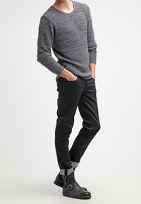 Suéter de punto texturizado gris, pantalones negros ajustados con dobladillos enrollados y botas negras hasta el tobillo con detalle de hebilla. Diseño minimalista.