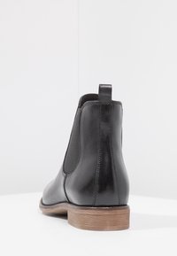 Botas de cuero negro hasta el tobillo con paneles laterales elásticos y una cinta para tirar, con punta redondeada y un tacón de madera. Textura suave.
