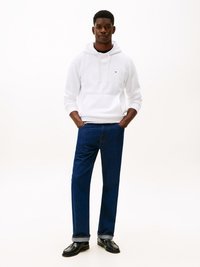 Vit hoodie med snörning, svart innerlager, blå denimjeans och svarta loafers. Modellen står mot en helt vit bakgrund.