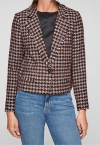 Tweedblazer i svart, rosa och vit rutmönster. Har en spetsig krage, tvåknappsstängning och texturerad tyg. Kombineras med blåjeans.