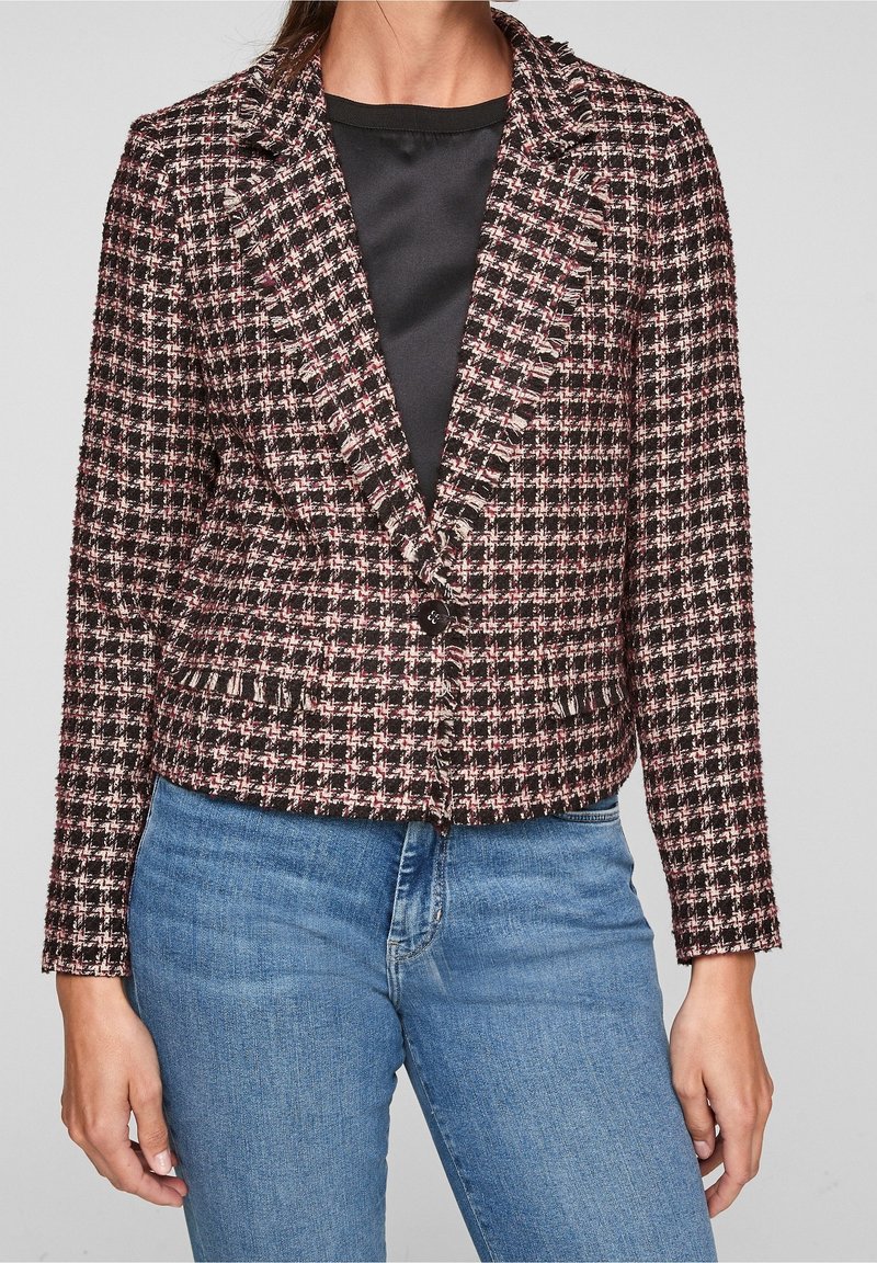 Tweedblazer i svart, rosa och vit rutmönster. Har en spetsig krage, tvåknappsstängning och texturerad tyg. Kombineras med blåjeans.