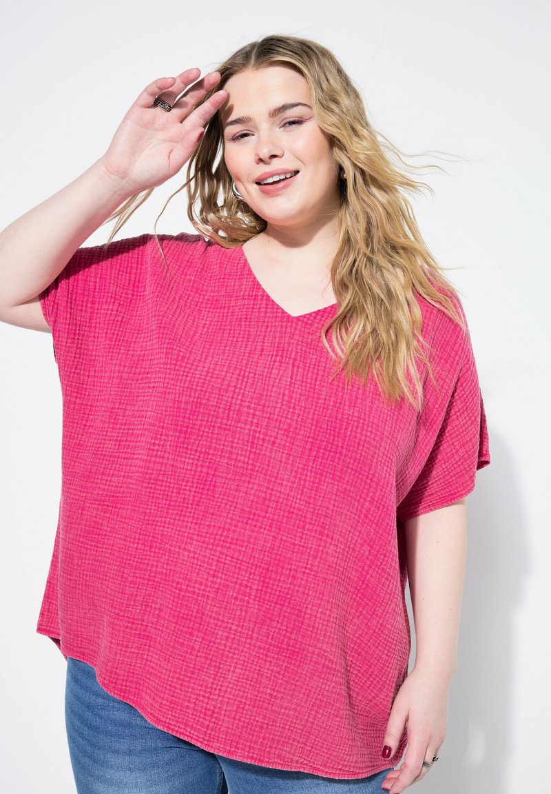 Top fucsia vivace e morbido con scollatura a V, realizzato in tessuto texturizzato. Maniche corte e orlo curvo, abbinato a jeans blu.