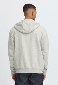 Gray hooded sweatshirt with a relaxed fit, featuring long sleeves, a drawstring hood, and ribbed cuffs and hem. Worn with dark denim jeans.