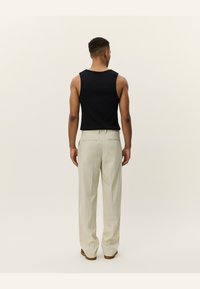 Black sleeveless top with a fitted design paired with light beige trousers, featuring a straight cut and subtle texture.