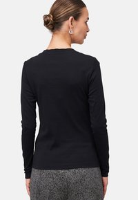 Zwarte longsleeve shirt met een ronde halslijn en een gladde textuur, van de achterkant weergegeven, gecombineerd met gestreepte grijze broek.