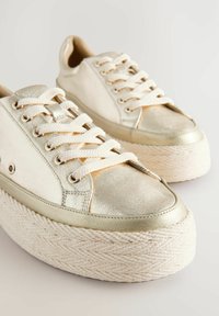 Baskets en toile doré métallisé et crème avec des semelles tissées épaisses, un design à lacets et des accents texturés contrastants sur le bout.