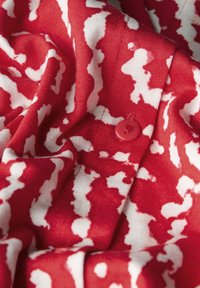 Tessuto rosso con un motivo astratto bianco e un dettaglio con bottone rosso, caratterizzato da una consistenza morbida e una finitura liscia.
