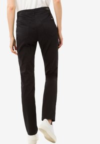 Pantaloni neri slim-fit con vita media, quattro tasche e finitura in tessuto liscio. Indossati con sneakers bianche.