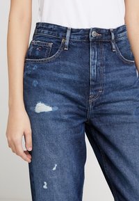 Mörkblå jeans med klassisk hög midja, med slitna detaljer och ljus blekning. Tillverkade av denim med en slät textur och fem fickor.