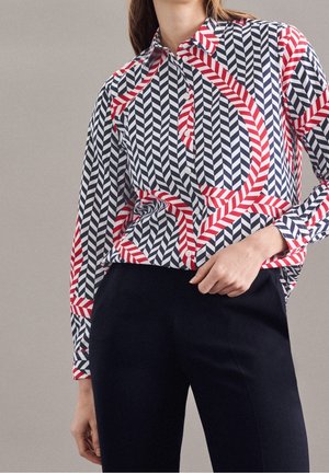 Chemise à boutons, avec un motif géométrique en chevrons rouge, marine et blanc, ainsi que des rayures. Manches longues, col et coupe décontractée.