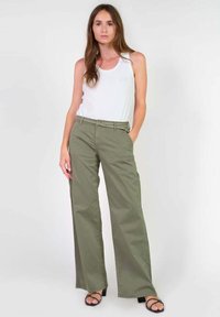 Lichte, wijde olijfgroene broeken met een gladde textuur, voorzien van een ritssluiting en knoopsluiting aan de voorkant. Vergezeld van een witte tanktop.