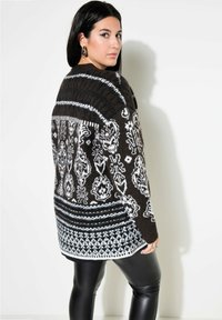 Brun och vit mönstrad tröja med en texturerad design, ribbad krage och långa ärmar, tillsammans med svarta leggings i konstläder.