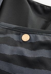 Črno-siv prožni tkanina z gladko teksturo, s krožnim logotipom v barvi bakra, ki je izpostavljen.