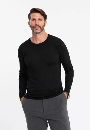 Pull noir à manches longues avec un col rond, en tissu tricoté léger, au design ajusté et aux poignets côtelés, associé à un pantalon gris.