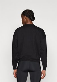 Czarna bluza z luźnym krojem, obniżonymi ramionami i ściągaczami. Gładka faktura i minimalistyczny design, bez widocznych wzorów.