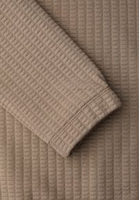 Tissu en maille côtelée beige avec un gros plan d'une manche repliée montrant des coutures détaillées et la texture.