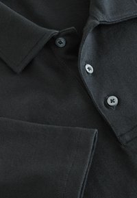 Sort polo shirt i et struktureret stof, med en foldet krave og to tydelige knapper langs lukningen. Enkel design.