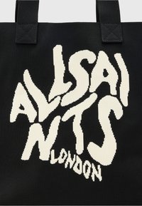 Grand sac fourre-tout en tissu noir, arborant une typographie ludique en blanc qui épelle "ALLSAINTS LONDON", avec des détails texturés sur l'ensemble.