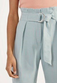 Kalhoty s vysokým pasem v světle modrém a bílém vzoru psa zuby, s stříbrnou kruhovou sponou a látkovým páskem. Hladká textura.