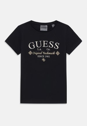 Zwarte katoenen T-shirt met witte geborduurde tekst "GUESS," "Original Trademark," en decoratieve accenten. Korte mouwen, basic ronde hals.